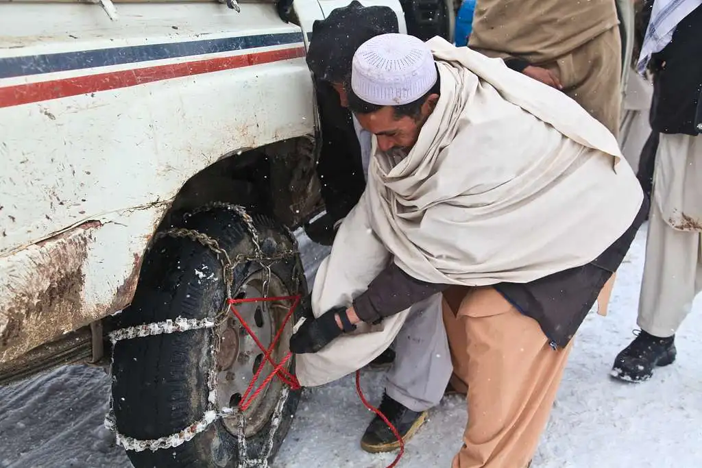 afghan men install snow chains around the tires
