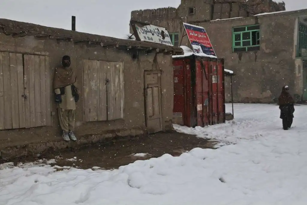 an afghan boy takes cover from the falling snow as